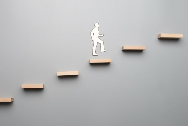 A grey background. There are 6 floating light wood shelves and a figure of a man using the shelves as stairs.