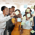 A group of office people smile and put up post-its on a trasnparent screen.