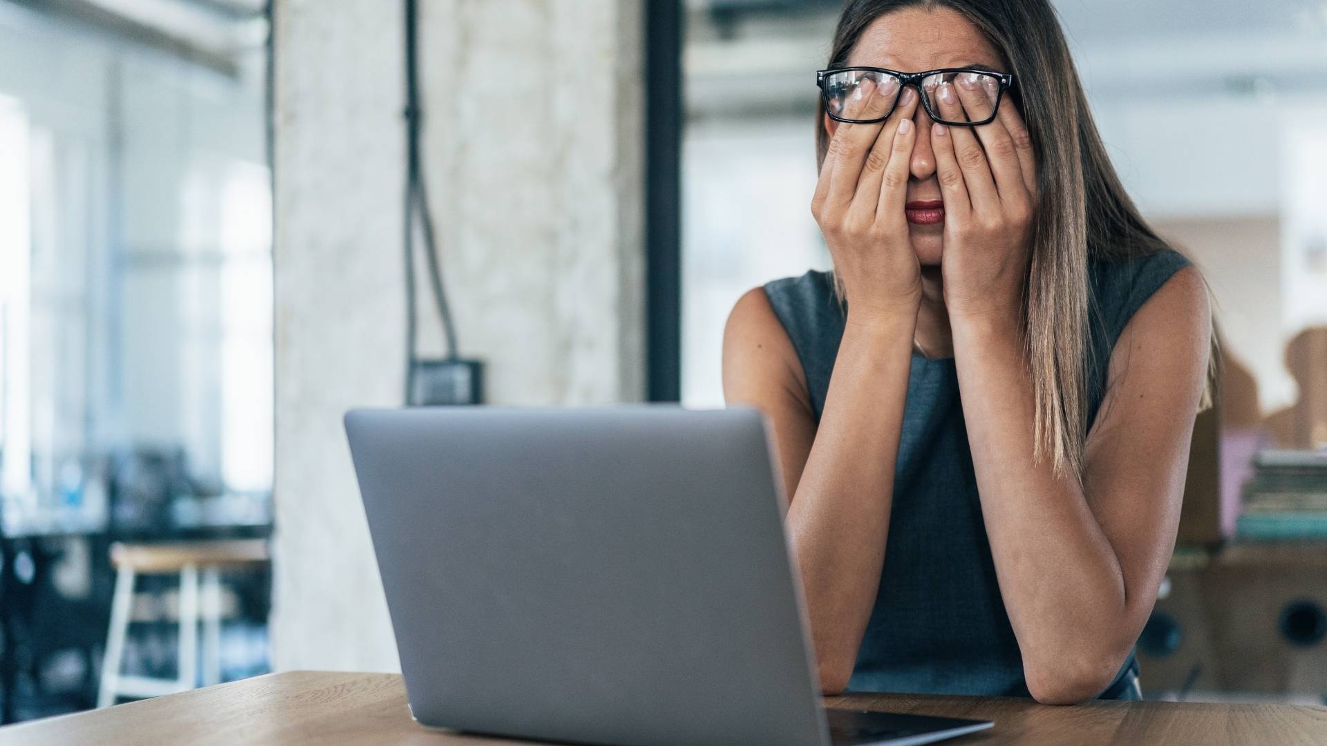 A tired office woman rubbing her eyes in front of her laptop