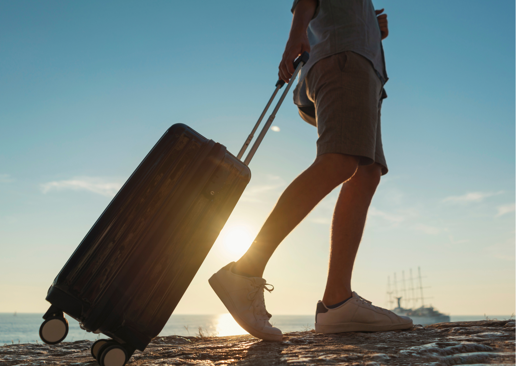 A person on a beach walking away with a bag. Sun and blue sky in the background.