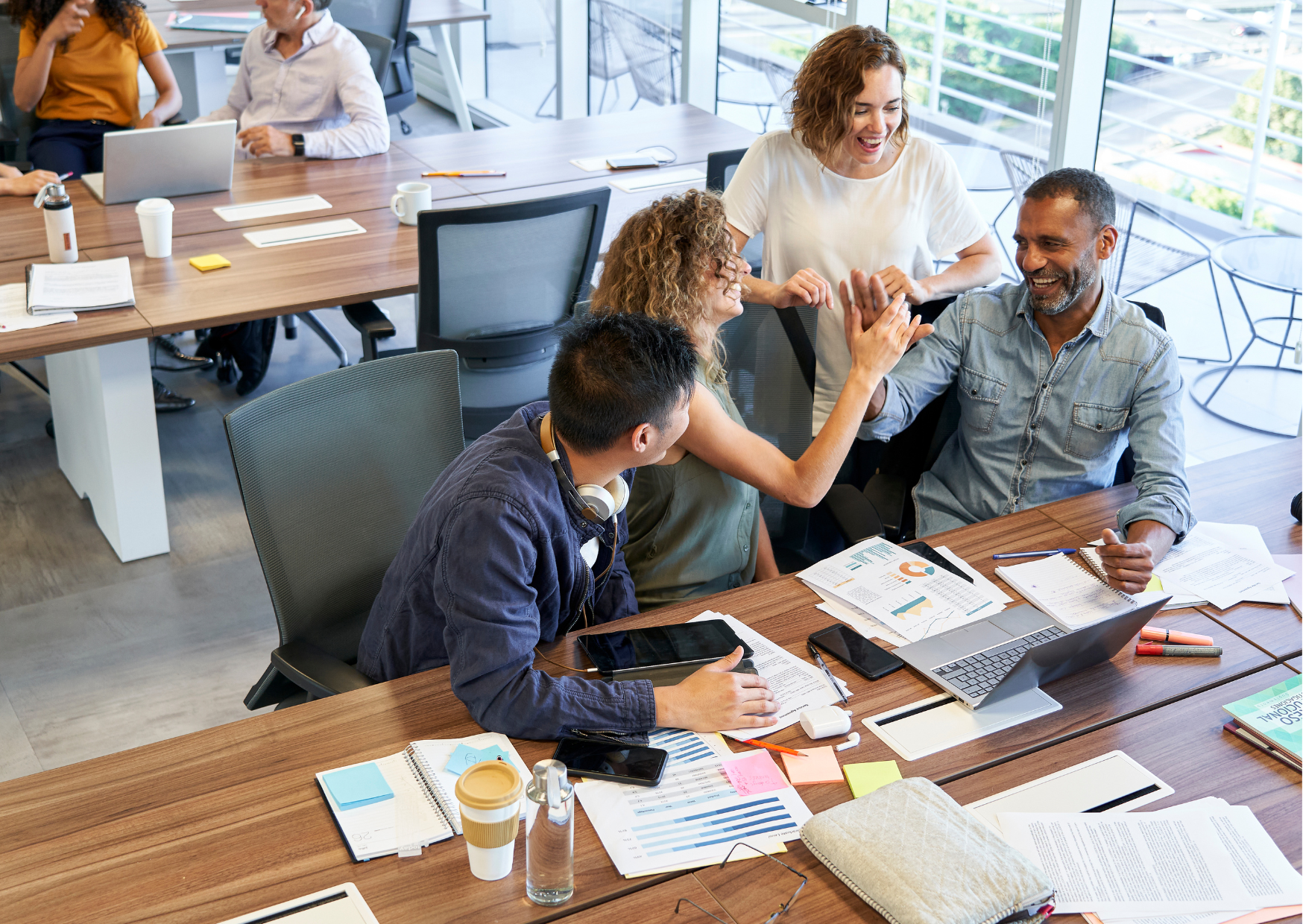 4 people at a wood desk in an office celebrating and high-fiving each other.