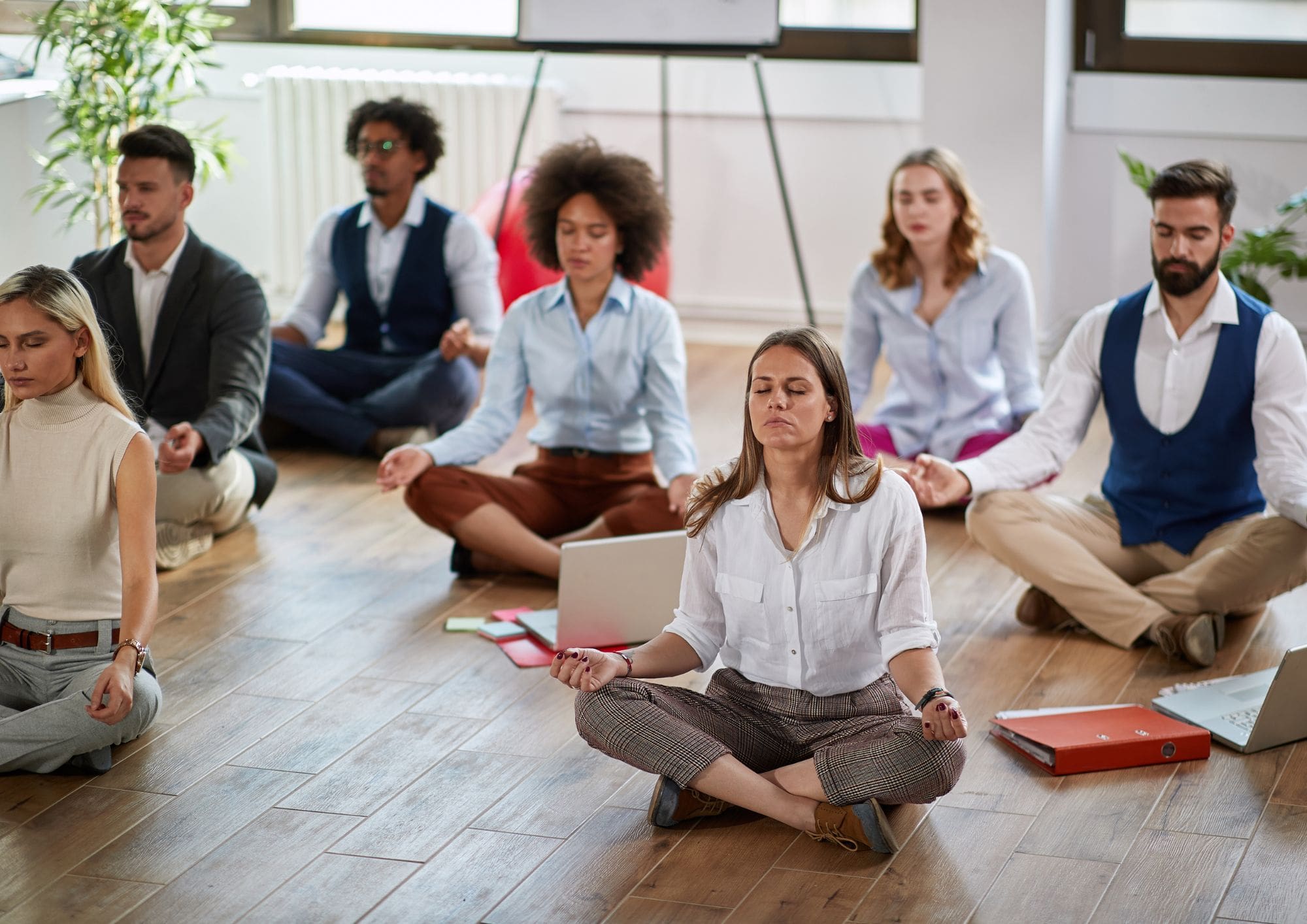 A group of business people meditating on the floor of a bright office.