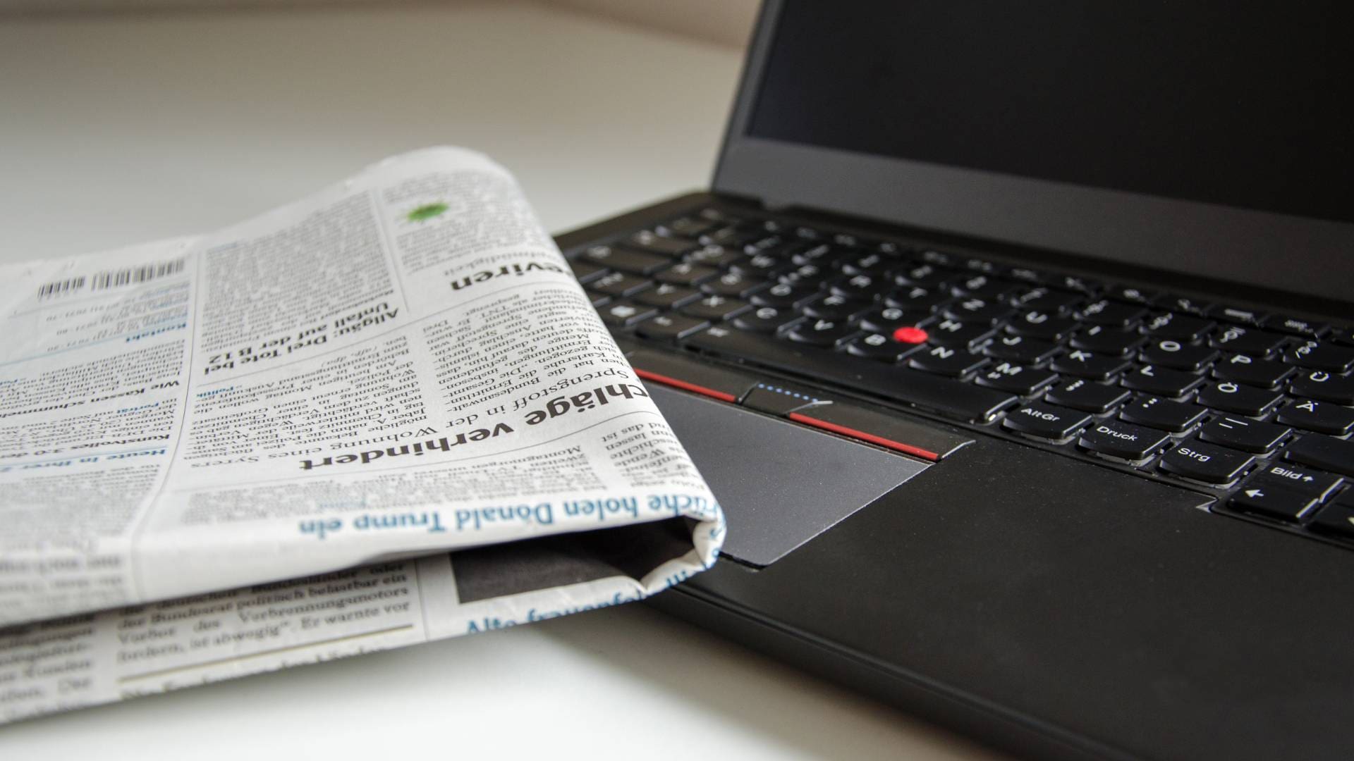 An open black laptop with a folded newspaper placed on top